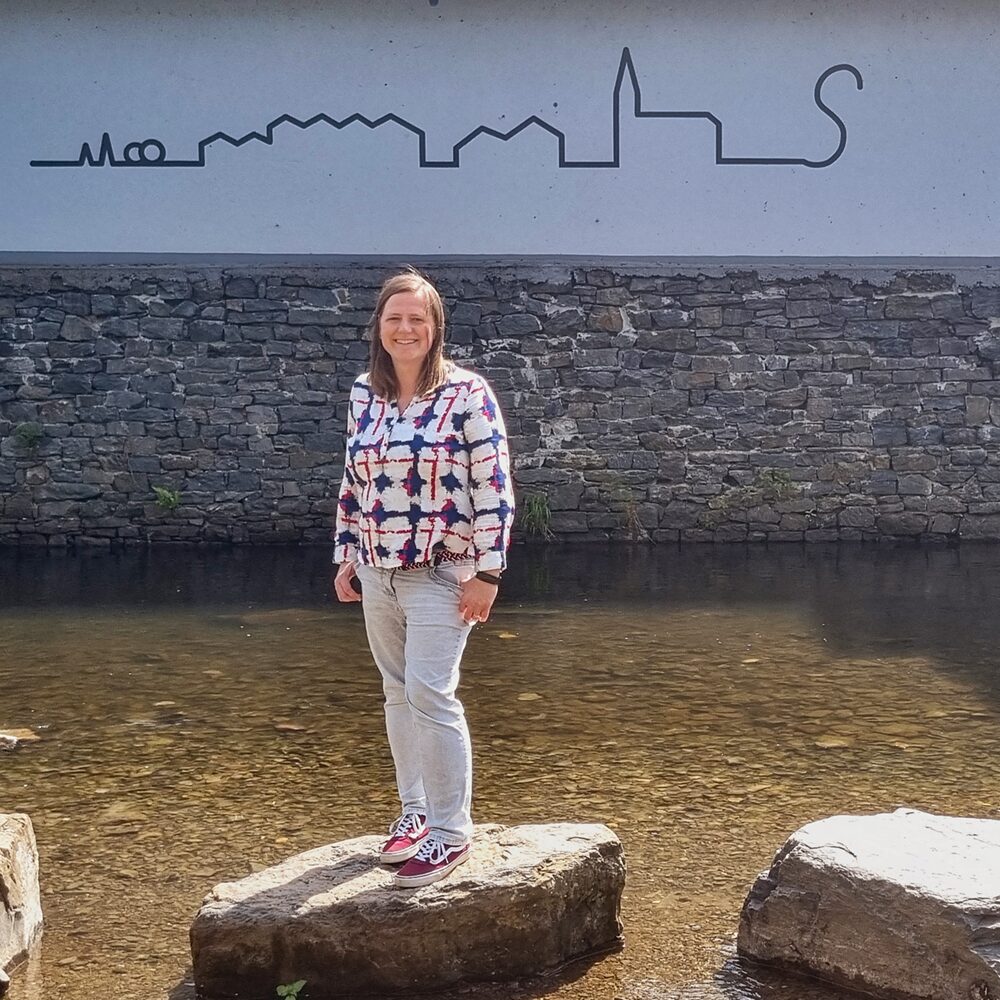 Denise Brilla steht in der Volme auf den großen Steinen im Hintergrund der Schriftzug Skyline Schalksmühle